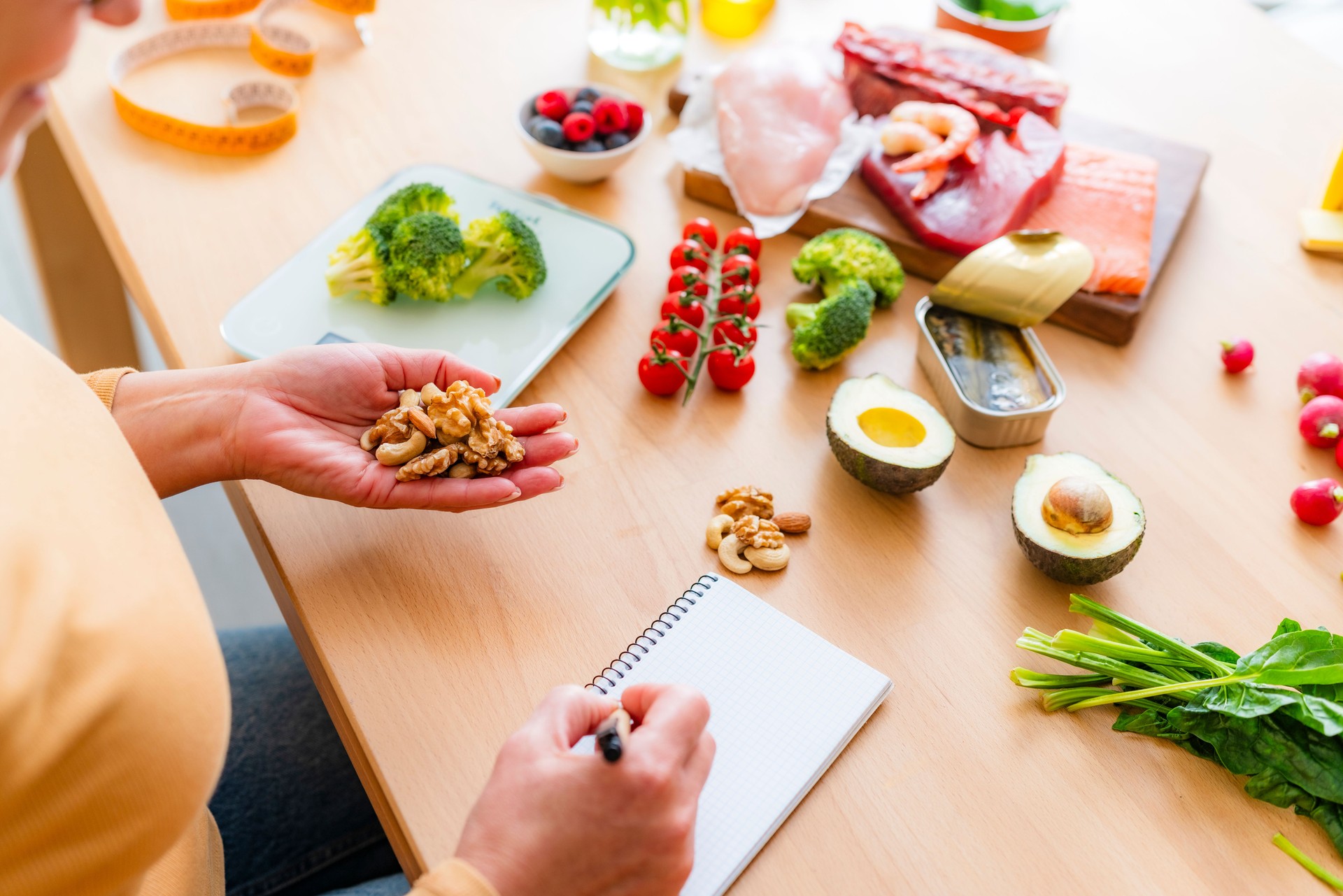 Woman planning a healthy low carb diet. She is taking notes of the right portion of food. Holding nuts and seeds and writing